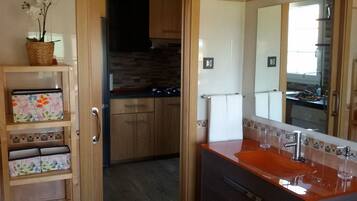 Ein modernes Badezimmer mit einem Holzkosmetikschrank, einem großen Spiegel und einem Waschbecken. Es gibt eine kleine Ablage mit einer dekorativen Schachtel und einer Topforchidee.