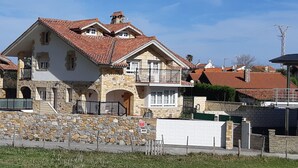 A two-story stone house with a red-tiled roof, a balcony, and a stone wall in front. - Exclusive apartment in beach Sonabia with a view to the sea and the mountain. (Castro Urdiales)