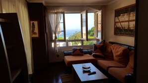 A living room with a sofa, a coffee table, and a view of the sea through large windows. - Exclusive apartment in beach Sonabia with a view to the sea and the mountain. (Castro Urdiales)