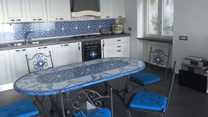 Una cocina con armarios blancos, baldosas con diseño azul y blanco, una estufa a gas, un lavamanos y un ventanal con vistas al follaje.