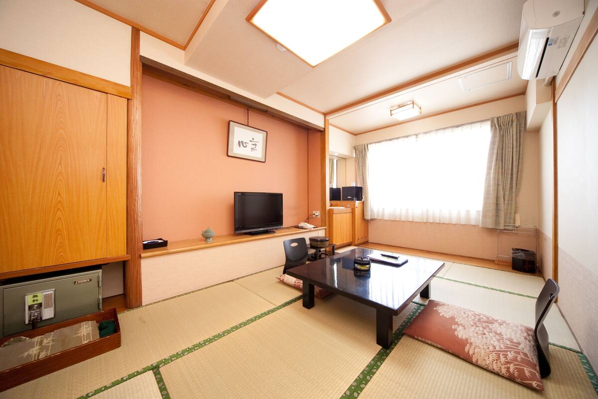 A traditional Japanese room with tatami flooring, a low table, a television, and a sliding door.