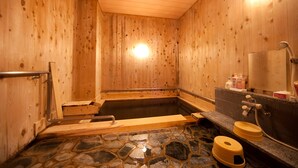 A wooden sauna with a stone floor, a wooden bench, and a bathtub.