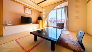 A modern hotel room with tatami mat flooring, a large glass table, a sofa, and a TV.