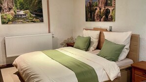 Un dormitorio con cama, mesita de noche, radiador y dos cuadros colgados en la pared.