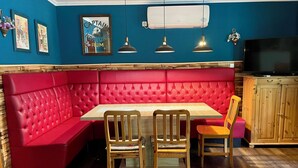Un comedor con un banco acolchado rojo, sillas de madera, una mesa de madera y un televisor sobre un mueble de madera.