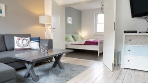 Una sala moderna con un sofá gris, una mesita de centro, un aparador blanco y una cama con colcha estampada en azul y verde.