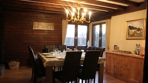 Un coin repas avec une table en bois dressée pour six personnes, entourée de chaises. Un lustre est suspendu au plafond et un tableau orne le mur.