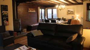 Un salon chaleureux avec une cheminée, un coin repas et un canapé en cuir noir.