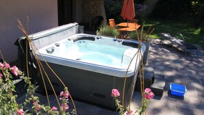 Un bain à remous installé dans un espace extérieur aménagé, avec un mur en pierre, du mobilier de jardin et des plantes en pot.