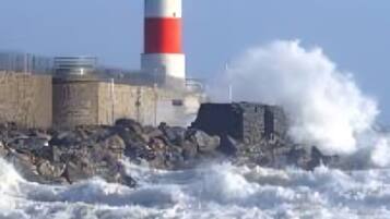 Un faro con franjas rojas y blancas, ubicado en una costa rocosa donde las olas golpean con fuerza.