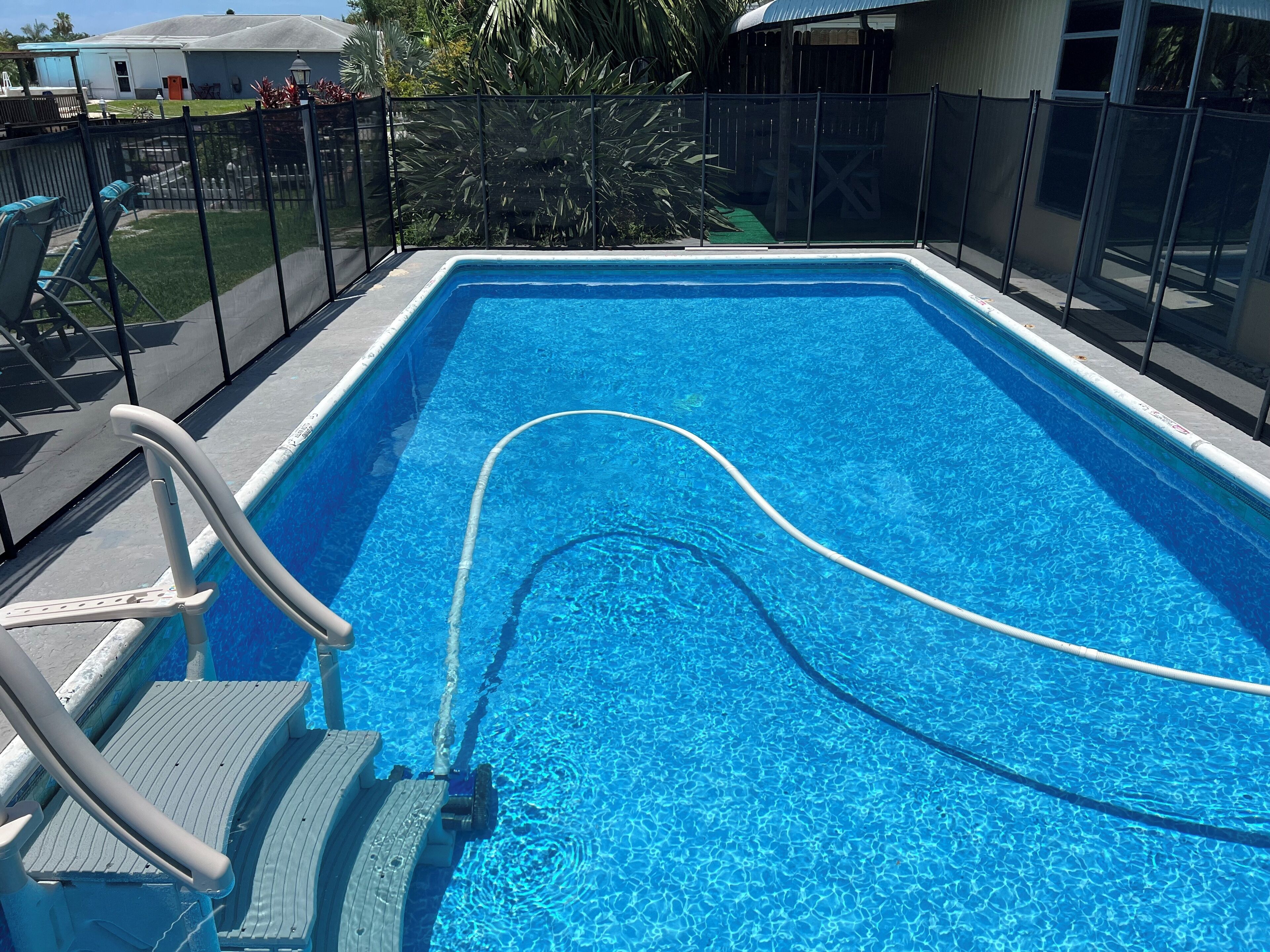 A rectangular swimming pool with clear blue water, surrounded by a black fence, and a pool ladder on the left side.