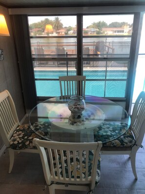 A glass-top dining table with chairs, a flower-patterned tablecloth, and a view of a swimming pool through large windows. - GREAT LOCATION WATERFRONT, HEATED POOL! BEAUTIFUL SUNSETS, ALL PETS STAY FREE! (Holiday)