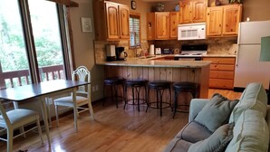 A cozy kitchen with wooden cabinets, a dining table with chairs, and a bar stool area. - Lakefront Adventure: Private Hot Tub,  Dock, Nearby Rafting, Biking & More! (Robbinsville)