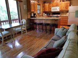 A cozy kitchen with wooden cabinets, a dining table with chairs, and a bar stool area. - Lakefront Adventure: Private Hot Tub,  Dock, Nearby Rafting, Biking & More! (Robbinsville)