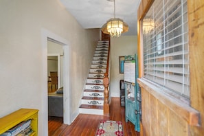 Staircase with ornate metal balusters and a chandelier above, flanked by a wooden door and a bookshelf.