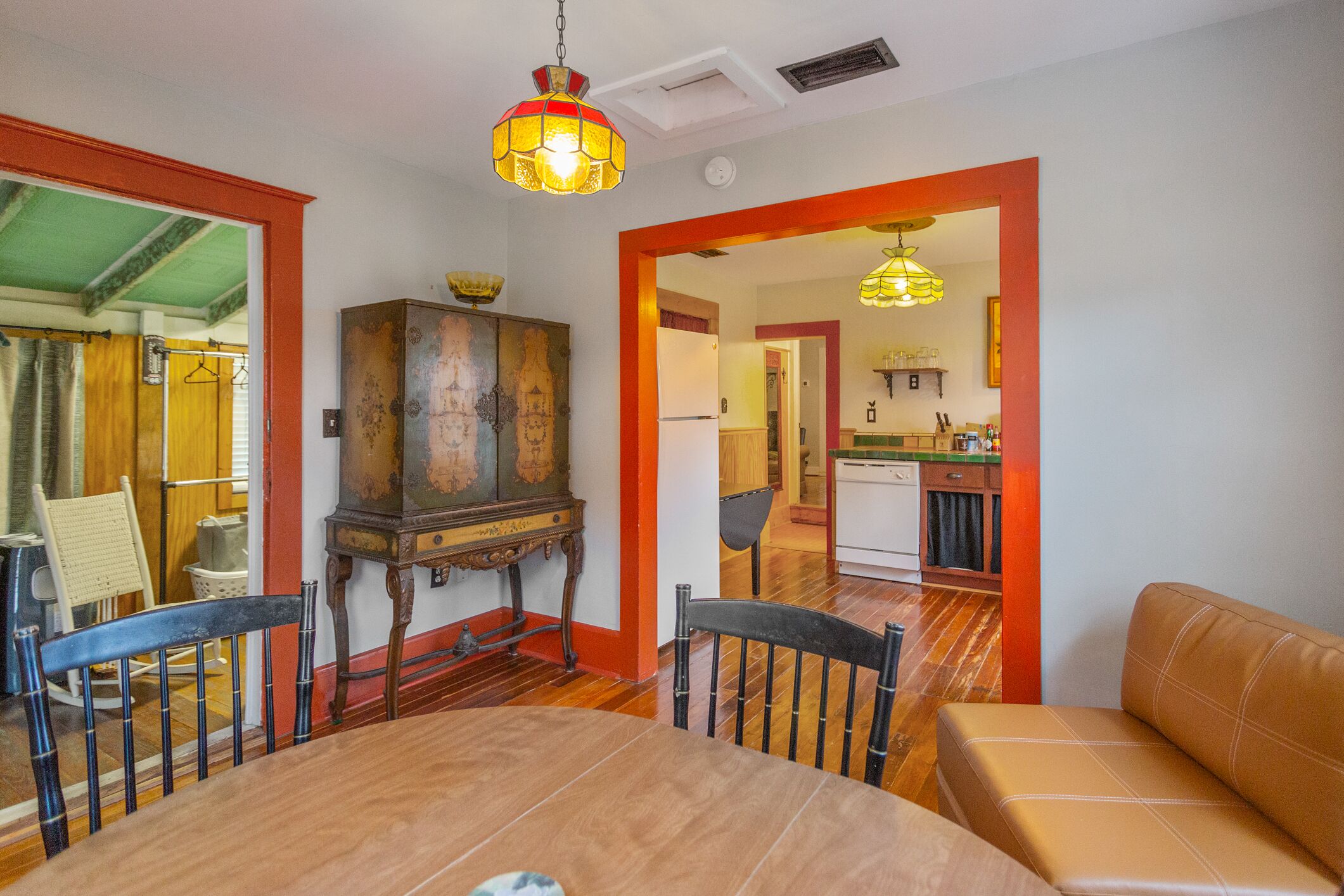 A dining area with a wooden table, chairs, and a sofa. There is a kitchen visible through an open doorway.