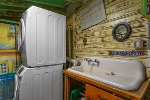 Relax in this charming bathroom with a washing machine, sink, and mural-adorned walls.