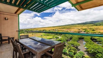 Ein Balkon mit Glastisch und Korbstühlen, der auf eine grüne Landschaft mit einer Straße und geparkten Autos blickt.