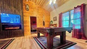 Un interior de madera con mesa de billar, televisor y chimenea.