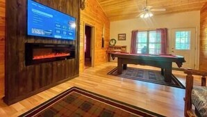 Una habitación con techo de madera, chimenea, mesa de billar y televisión montada en la pared.