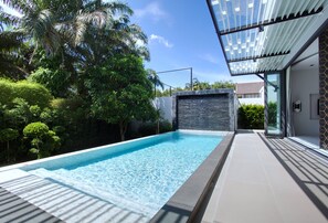 A modern swimming pool with a stone wall and glass doors, surrounded by lush greenery and a clear blue sky. - Picasso Villa Phuket - Pablo (Choeng Thale)
