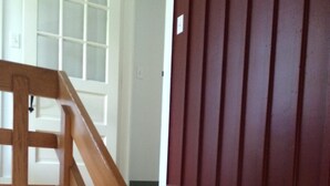 Una escalera de madera con barandilla, que conduce a un cuarto con pared blanca y panel de madera oscura.