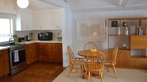Una cocina con armarios de madera, una mesa de comedor con sillas, un microondas y un hervidor.