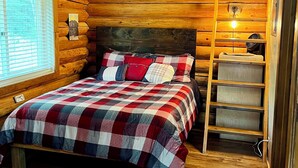 A cozy log cabin room with a bed, a wooden ladder, and a window with blinds. - Comfy Cabin Nestled in the Woods (Houston)