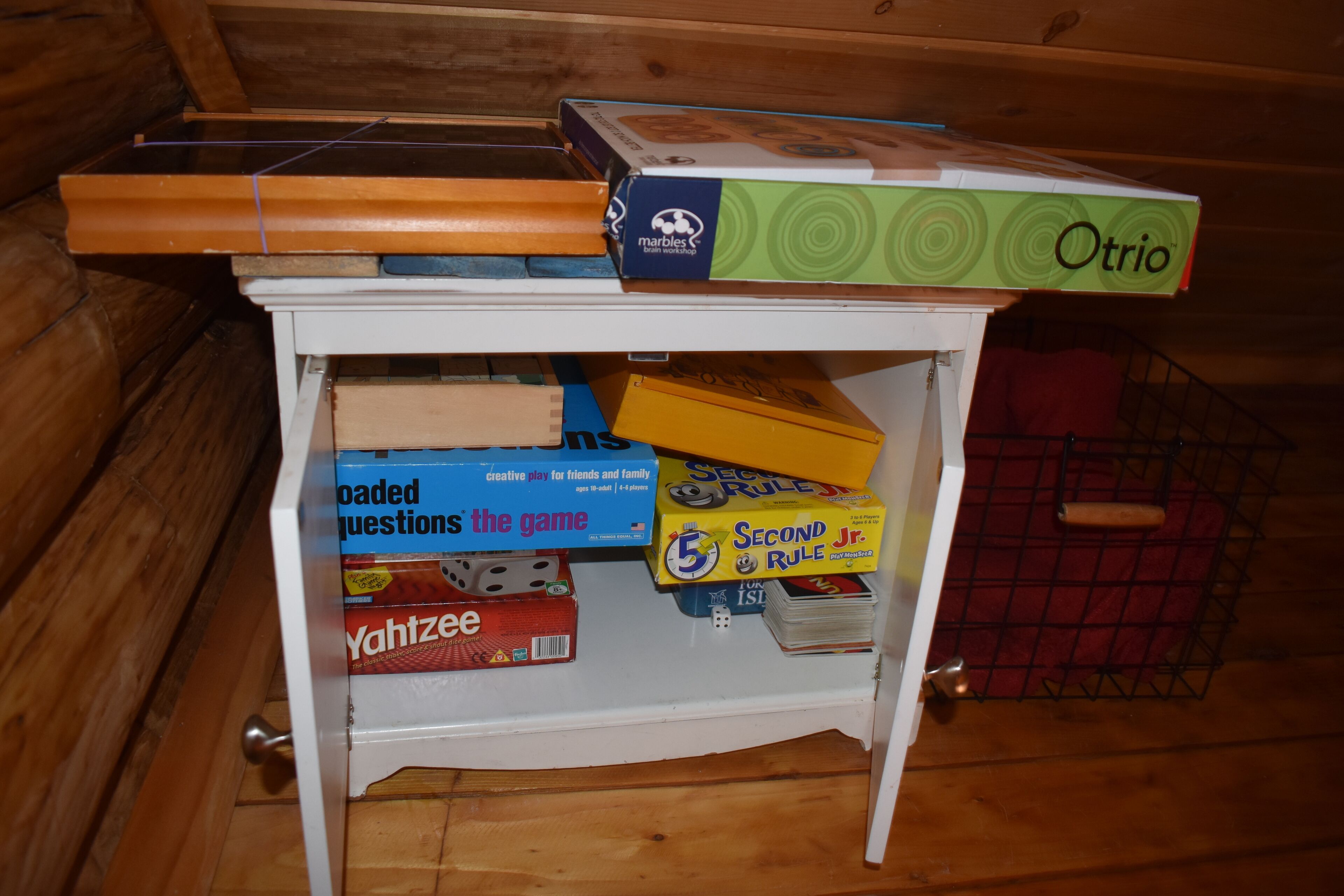 Une table en bois sur laquelle sont disposés divers jeux de société, avec une petite étagère en dessous.