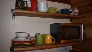 A kitchen shelf with various mugs and a microwave. - Comfy Cabin Nestled in the Woods (Houston)