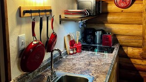 A kitchen with a granite countertop, stainless steel sink, hanging pots, and a clock on the wall. - Comfy Cabin Nestled in the Woods (Houston)