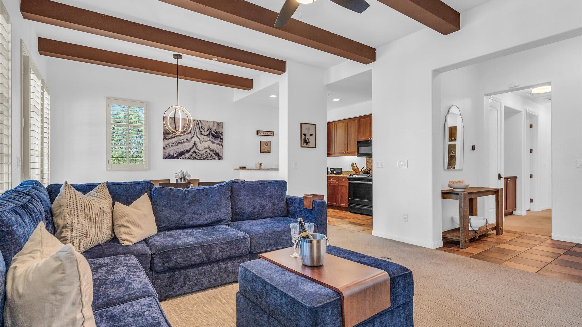 Uma sala de estar moderna com um sofá azul, uma mesa de centro de madeira e uma cozinha ao fundo.
