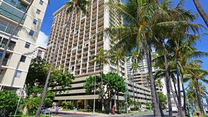 Un hôtel à plusieurs étages doté d’une architecture moderne, avec des balcons à chaque niveau et entouré de palmiers.