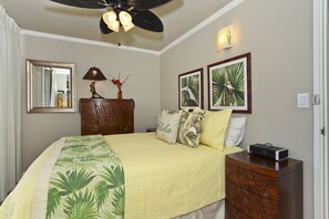 Un dormitorio con cama, mesita de noche, cómoda, ventilador de techo, espejo y cuadros con imágenes de plantas tropicales en la pared.