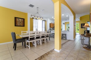 Uma sala de jantar com uma mesa e cadeiras brancas, uma cozinha ao fundo e paredes amarelas.