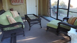 A sunlit patio with wicker furniture, a glass table, and a 'NO WAKE' sign on the wall.