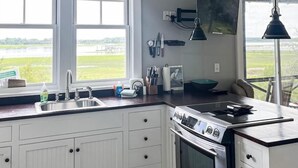 A modern kitchen with white cabinets, a stainless steel stove, and a large window overlooking a green landscape.