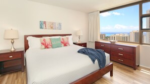 Een hotelkamer met een groot bed, een houten hoofdbord, twee nachtkastjes met lampen, en uitzicht op de stad door een groot raam, met een stadsgezicht buiten.