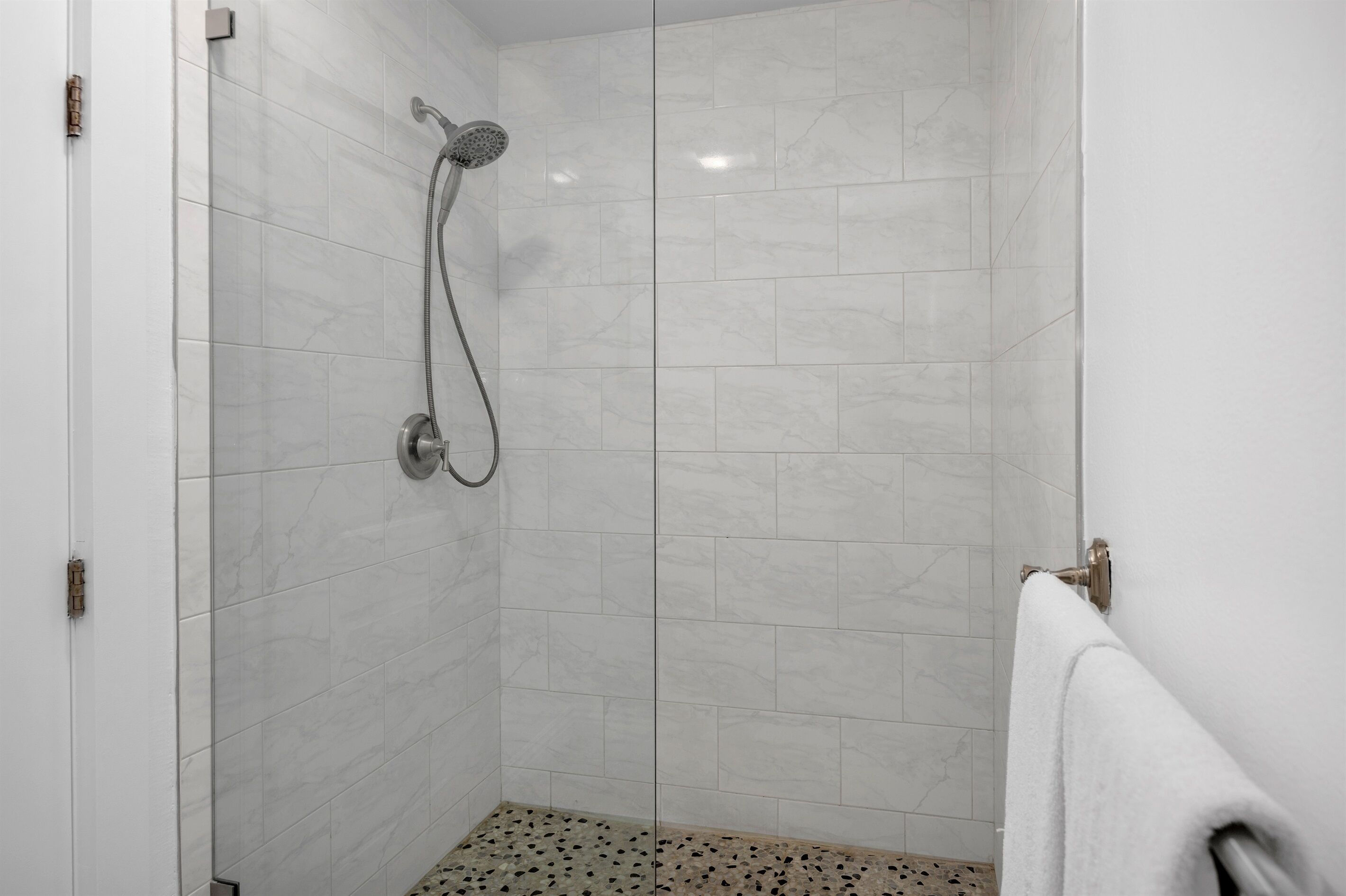 Une petite salle de bain moderne, avec des carreaux de marbre blanc, une douche équipée d’un pommeau de douche à main et un porte-serviettes.