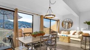 A modern living room with a dining area, large windows, a chandelier, and a view of the city.