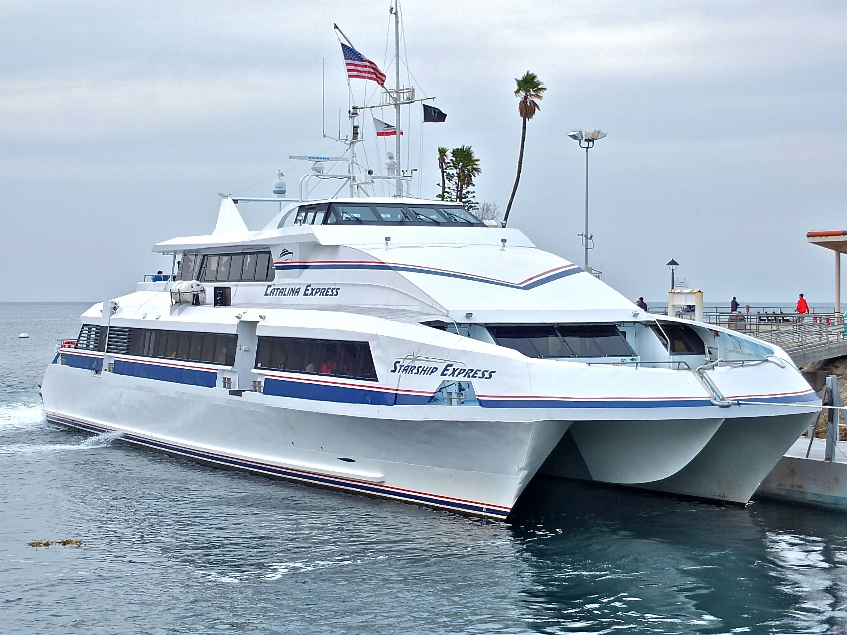 Eine große weiße Yacht namens 'Catalina Express' liegt an einem Steg, mit freiem Blick auf den Ozean und ein paar Palmen im Hintergrund.