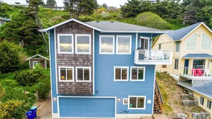 Ein zweistöckiges Haus mit blauer Garagentür, einem Balkon und einem kleinen Gartenhaus im Hinterhof.