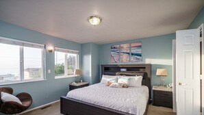 Ein Schlafzimmer mit einem großen Bett, zwei Nachttischen, einem Sessel und einem Fenster mit Jalousien.