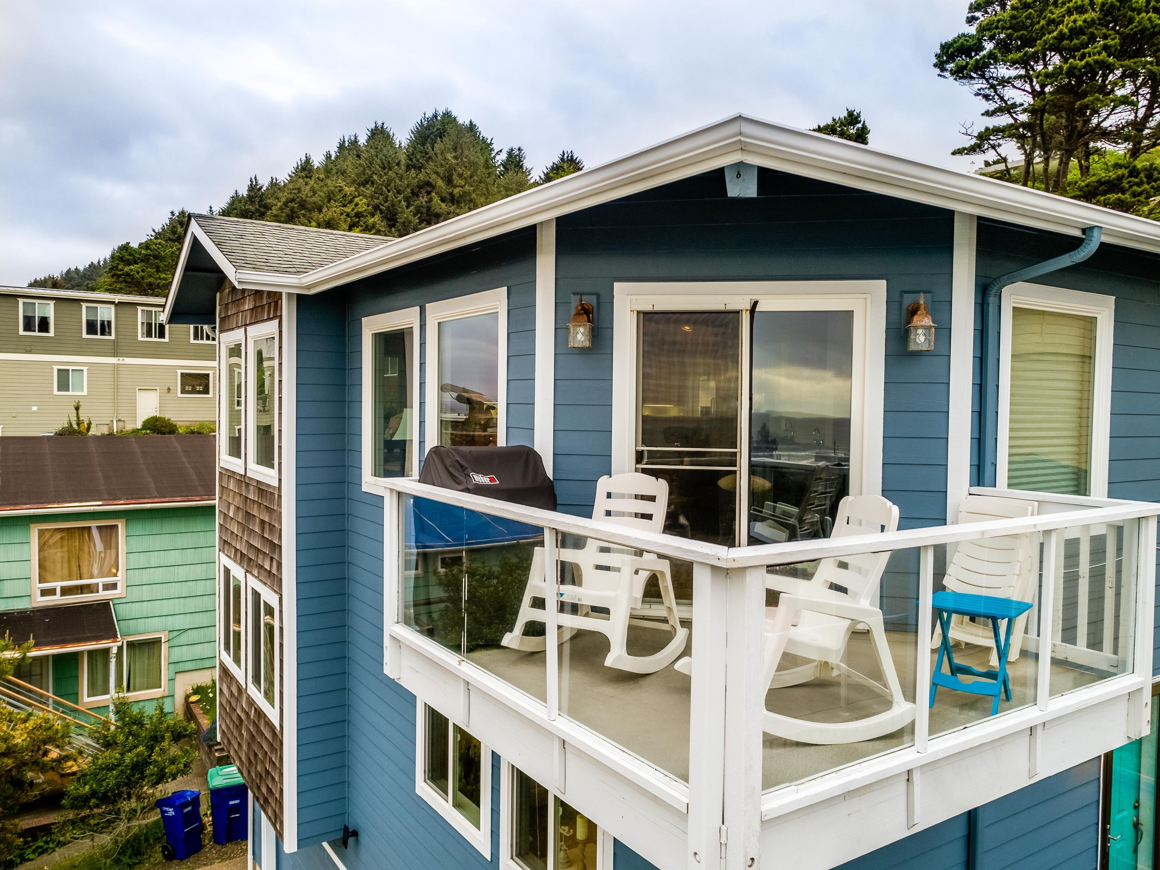 Une maison bleue dotée d’un balcon avec des chaises blanches et un barbecue.
