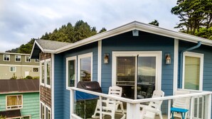 Ein blaues Haus mit Balkon, ausgestattet mit weißen Stühlen und einem Grill.