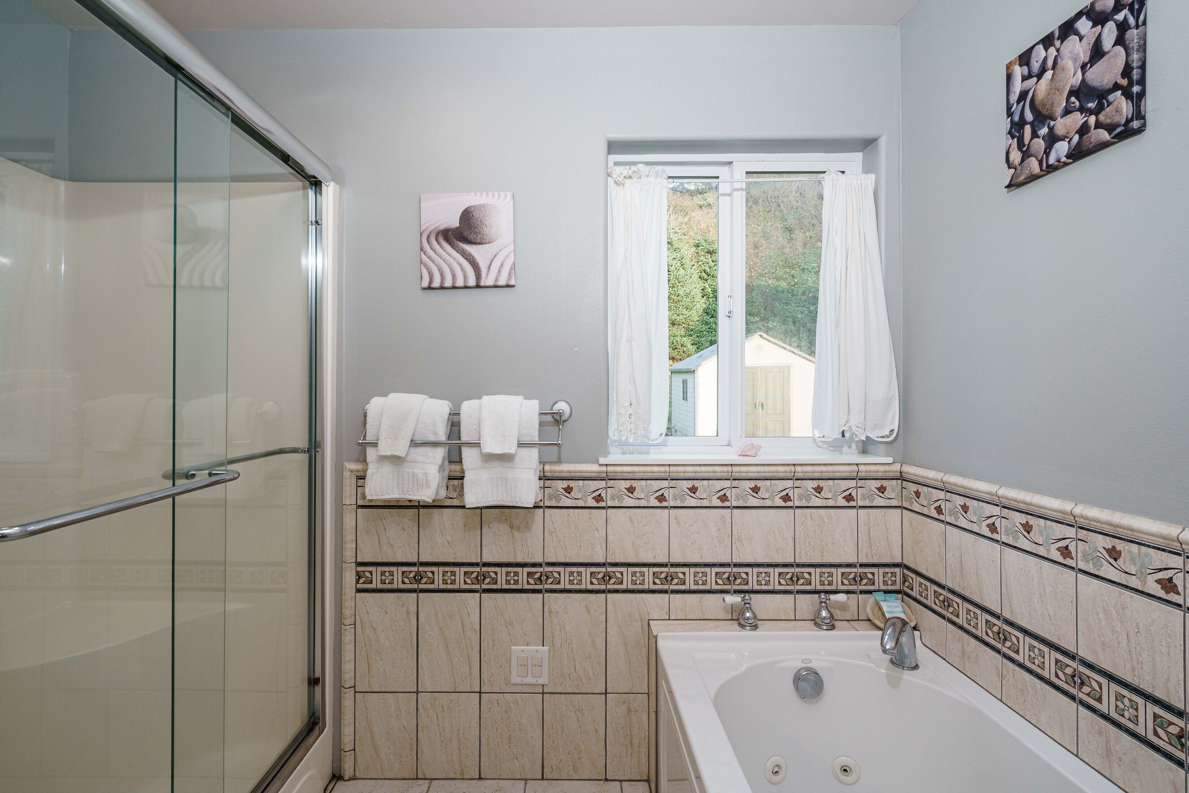 Ein Badezimmer mit Duschkabine aus Glas, einer Badewanne und einem Fenster mit Blick auf Grünflächen.