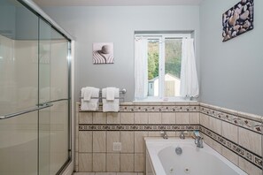 Un baño con cabina de ducha de vidrio, bañera y ventana con vistas a zonas verdes.
