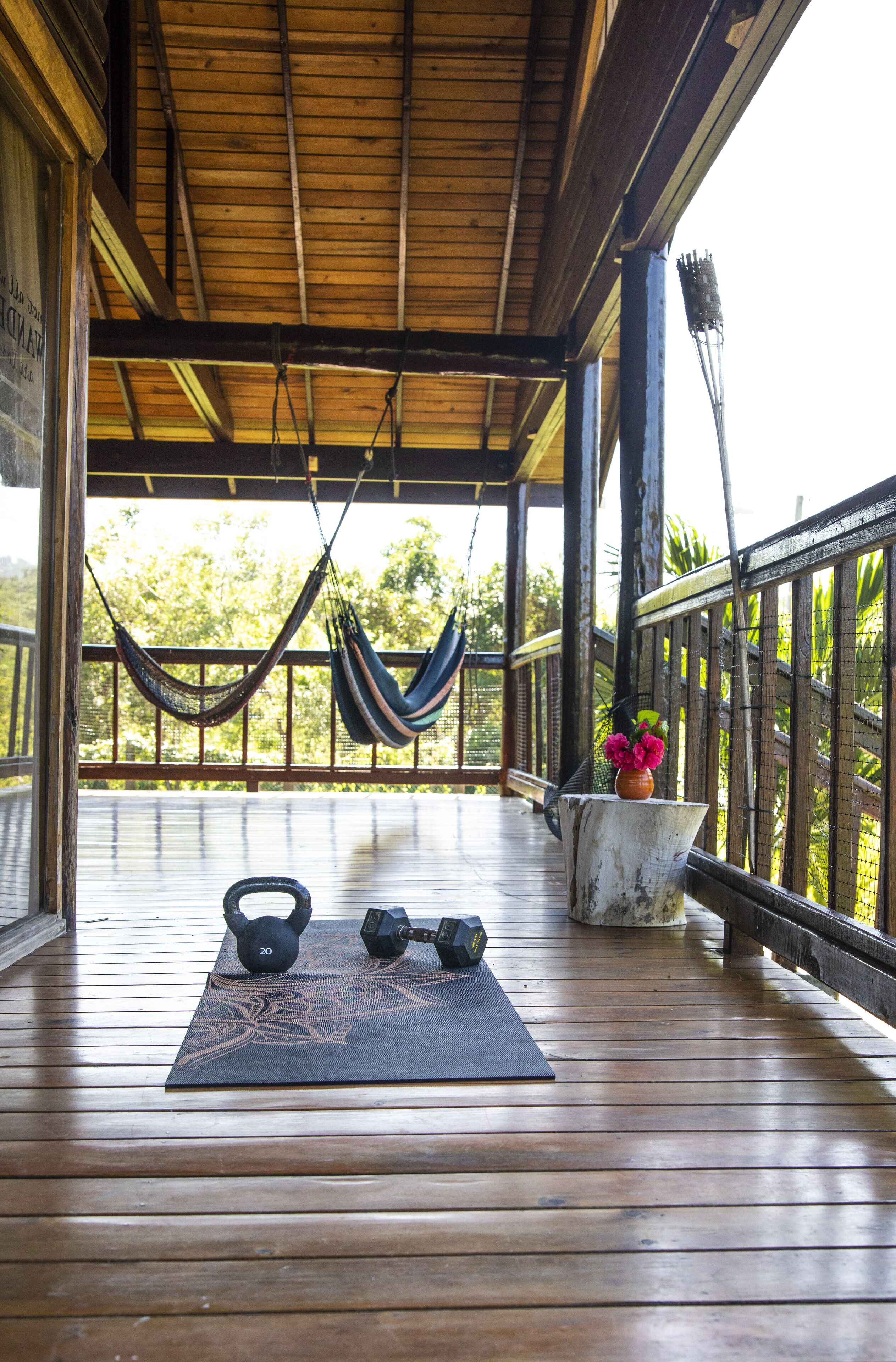 Eine Holzterrasse mit einer Hängematte, Yogamatte und Kurzhanteln.