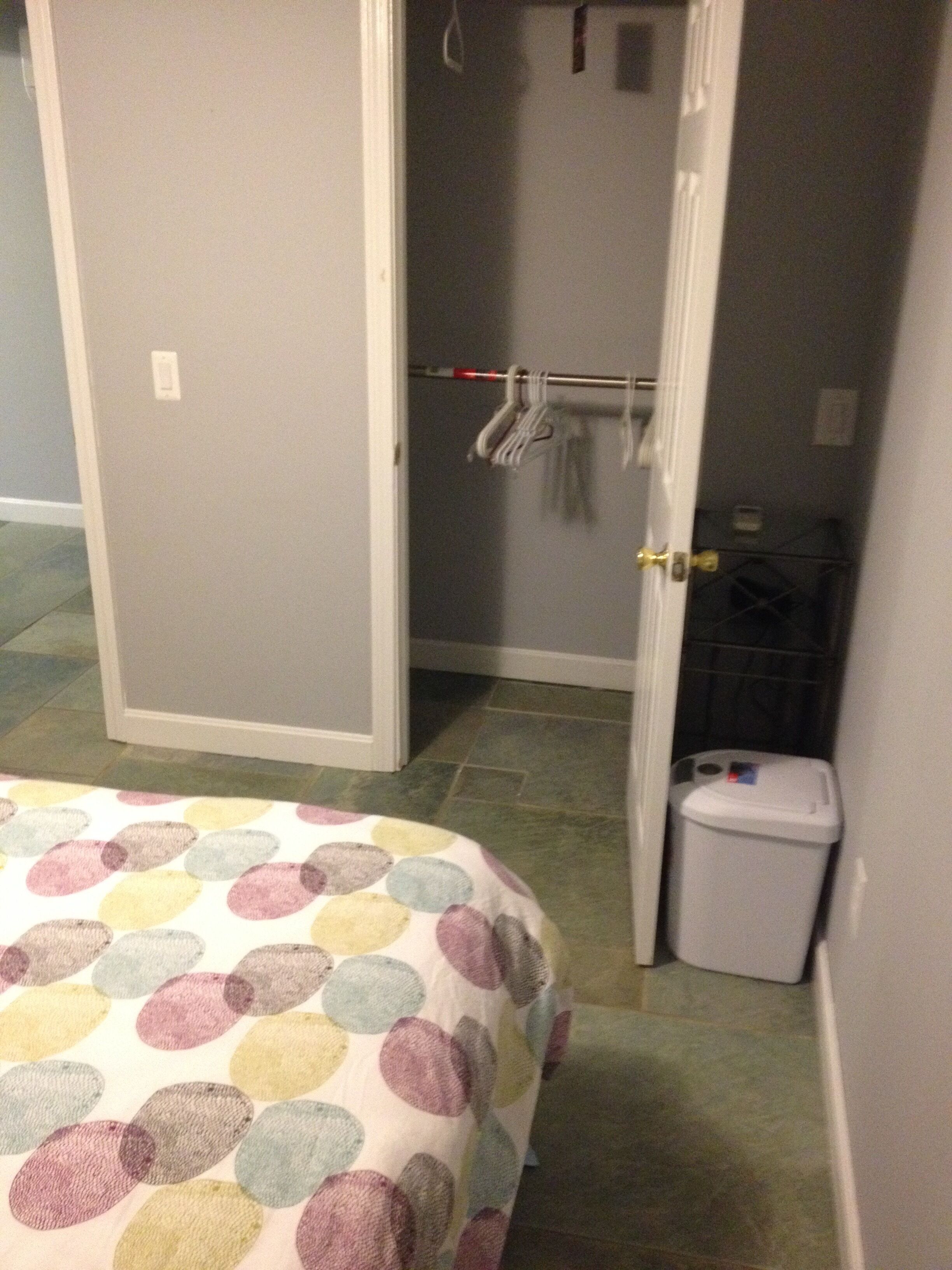 Une chambre à coucher avec un lit, une porte, un porte-manteau et une poubelle.