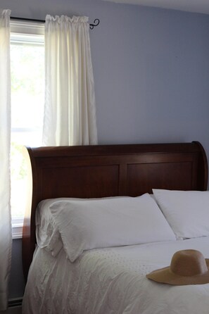 A bed with white linens, a wooden headboard, and a straw hat on the bed.